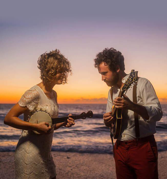 Man and woman standing on a beach playing instruments
