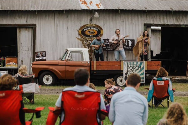 3 people playing and singing in the back of a vintage truck with an audience on a green